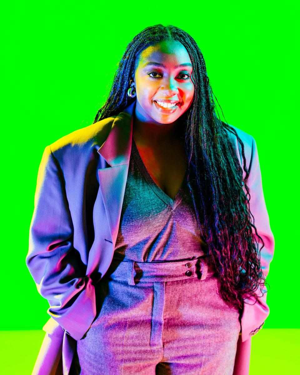 Lindsay People smiles while wearing a blazer against a neon green background.
