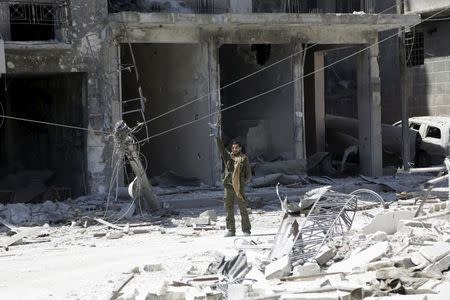 A rebel fighter carrying his weapon gestures at a site damaged by what activists said was shelling by warplanes loyal to Syria's President Bashar al-Assad in Jisr al-Shughour town, after the rebels took control of the area, April 26, 2015. REUTERS/Khalil Ashawi