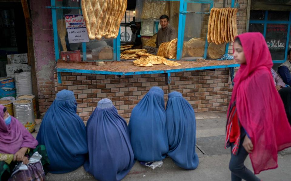 Burqa-clad women wait for free bread in front of a bakery in Kabul - BULENT KILIC /AFP