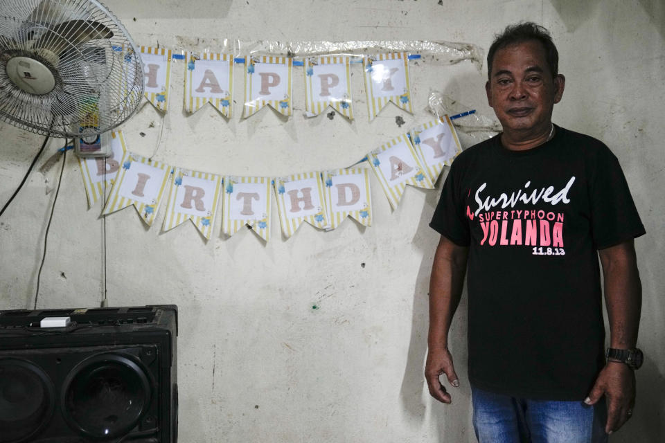 Reinfredo Celis poses on Monday, Oct. 24, 2022, beside a birthday sign placed by his friends last year in his home at a relocation site for victims of super Typhoon Haiyan in Tacloban, central Philippines. Celis, whose wife and brother died in the typhoon that hit on his birthday, says, "What is painful is I’m now alone.” (AP Photo/Aaron Favila)