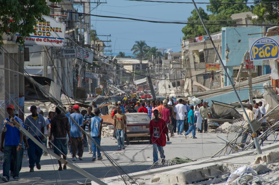 People wander the streets in front of the remains of a boarding school in the downtown area January 13, 2010 in Port-au-Prince, Haiti. / Credit: Frederic Dupoux / Getty Images