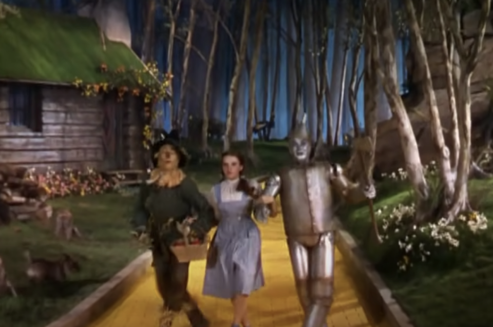 A bird behind the Scarecrow, Dorothy, and the Tin Man on the yellow brick road