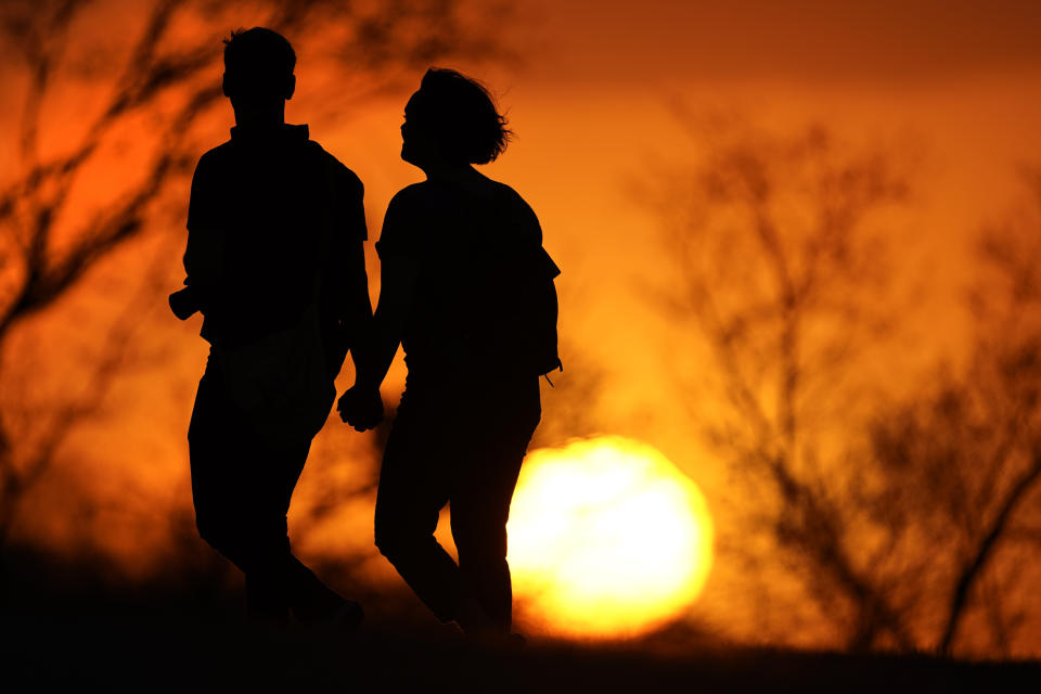 FILE - In this Wednesday, March 10, 2021 file photo, a couple walks through a park at sunset, in Kansas City, Mo. While most Americans have weathered the pandemic financially, about 38 million say they are worse off now than before the outbreak began in the U.S. According to a new poll from Impact Genome and The Associated Press-NORC Center for Public Affairs Research 55% of Americans say their financial circumstances are about the same now as a year ago, and 30% say their finances have improved. (AP Photo/Charlie Riedel, File)