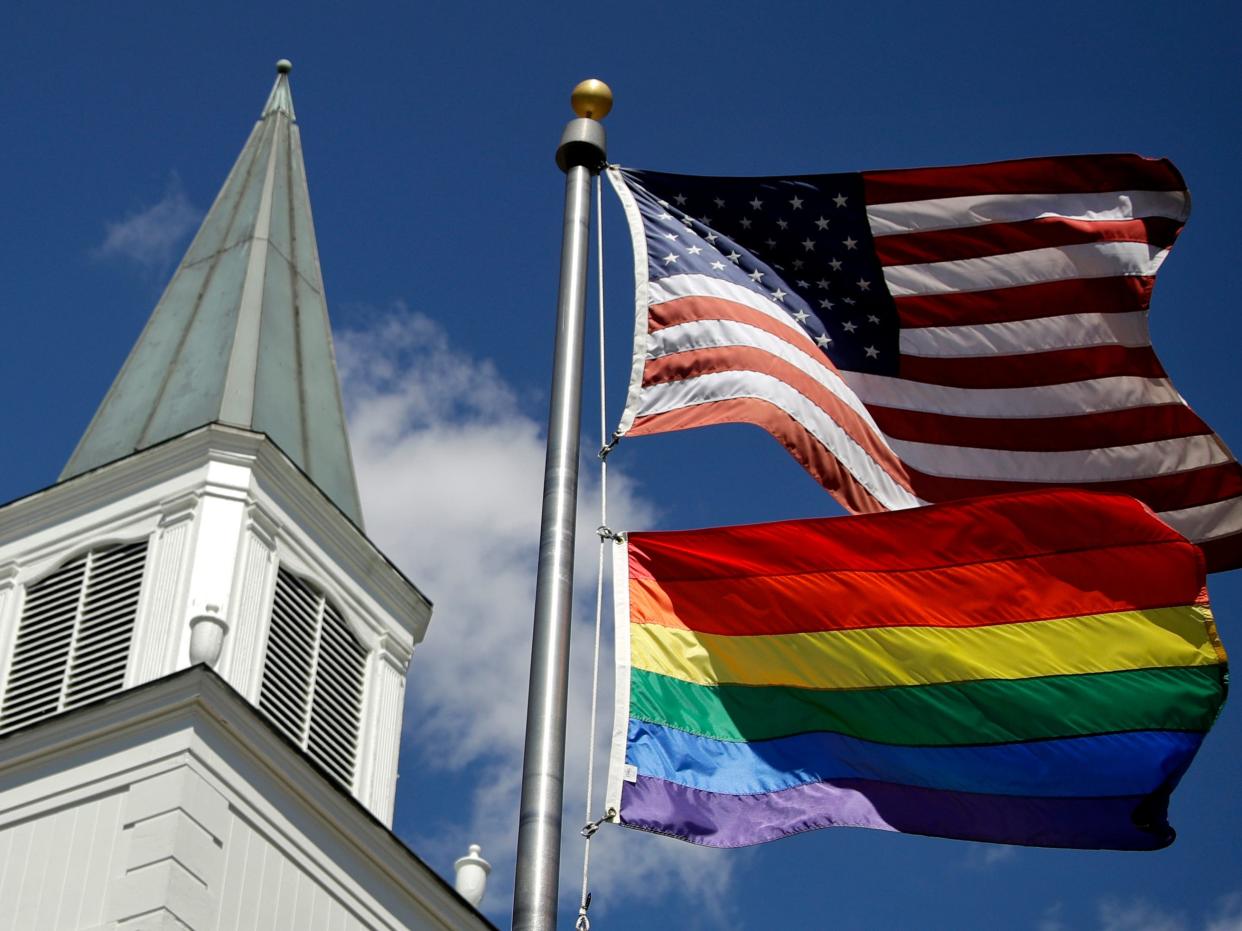 FILE - In this April 19, 2019 file photo, a gay pride rainbow flag flies along with the U.S. flag in front of the Asbury United Methodist Church in Prairie Village, Kan. Had there been no COVID-19 coronavirus pandemic, America’s largest mainline Protestant denomination would be convening in May 2020 for a likely vote on breaking up over differences on same-sex marriage and ordination of LGBTQ pastors. (AP Photo/Charlie Riedel, File)