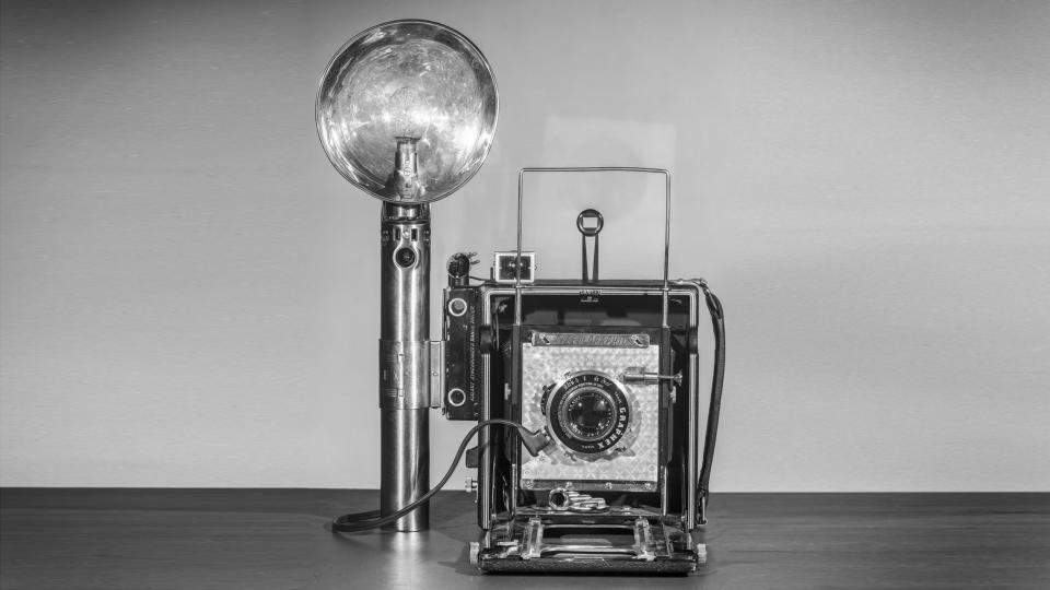 A Graflex Speed Graphic camera, with flash.