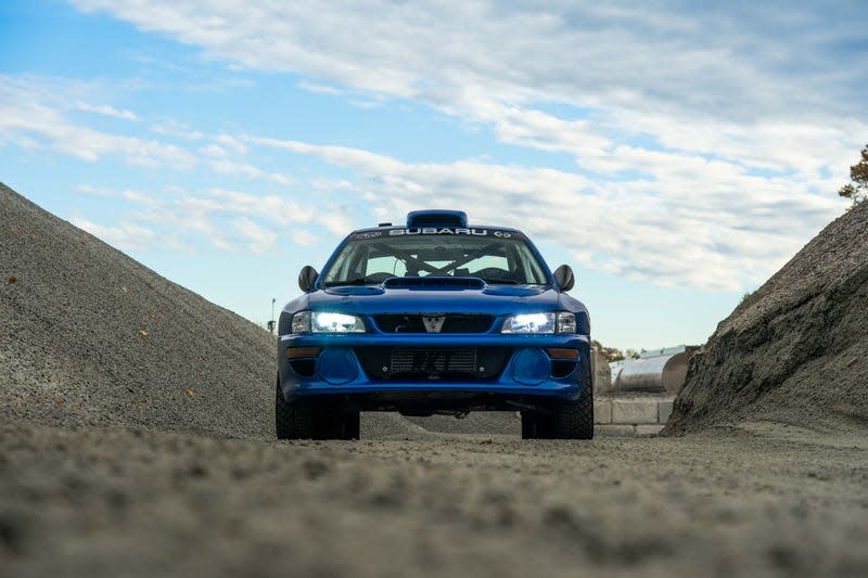 front-end view of a blue subaru coupe parked among piles of gravel in an industrial lot
