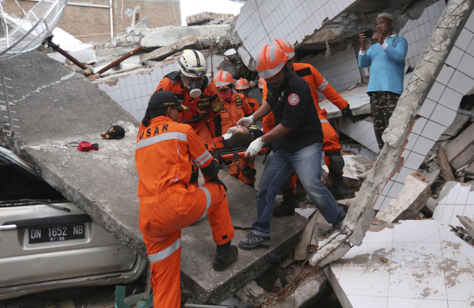 In this Sunday, Sept. 30, 2018, file photo, rescuers carry a survivor rescued from a restaurant building damaged by a massive earthquake and a tsunami in Palu, Central Sulawesi, Indonesia. (AP Photo/Tatan Syuflana, File)