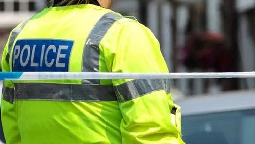 A police cordon with the back of a police officer's hi-vis jacket