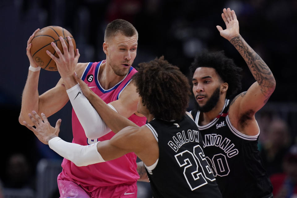 Washington Wizards center Kristaps Porzingis, left, attempts to pass around San Antonio Spurs forwards Dominick Barlow (26) and Julian Champagnie (30), during the second half of an NBA basketball game Friday, March 24, 2023, in Washington. (AP Photo/Carolyn Kaster)