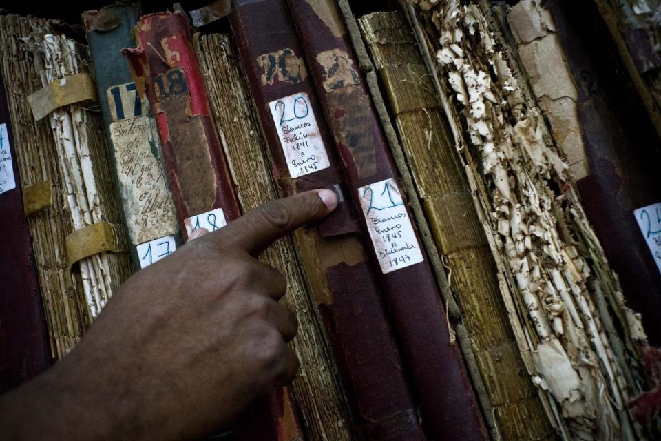 This Jan. 12, 2017 photo shows a man searching among volumes labeled "Whites" as part of an effort to digitize colonial-era registries of blacks and whites at the Espiritu Santo Church in Old Havana, Cuba. "That's how these books where placed, books for whites, books for blacks. The important thing is to preserve as many of them as possible," said church Deacon Felix Knights. (AP Photo/Ramon Espinosa)