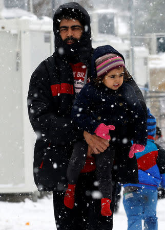Stranded Syrian refugee carries his child through a snow storm at a refugee camp north of Athens, Greece January 10, 2017.REUTERS/Yannis Behrakis