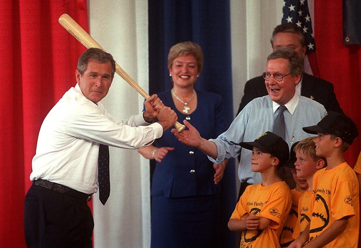 Texas Gov. and presidential hopeful George W. Bush goes to bat Friday, July 23, 1999, with a Louisville Slugger baseball bat given to him by a YMCA little league team as Bush greets supporters in Louisville, Ky., on his way to a $1,000 a plate private fundraiser. U.S. Sen. Mitch McConnell, R-Ky, in blue shirt, stands behind the little league team looking on. 