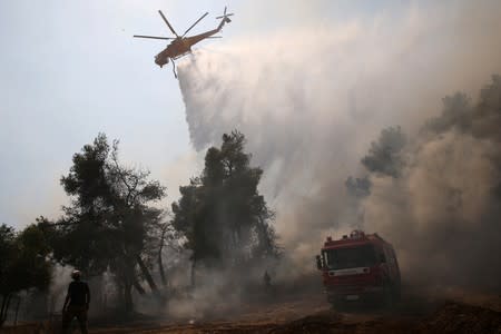 A firefighting helicopter makes a water drop as a wildfire burns in the village of Makrimalli on the island of Evia