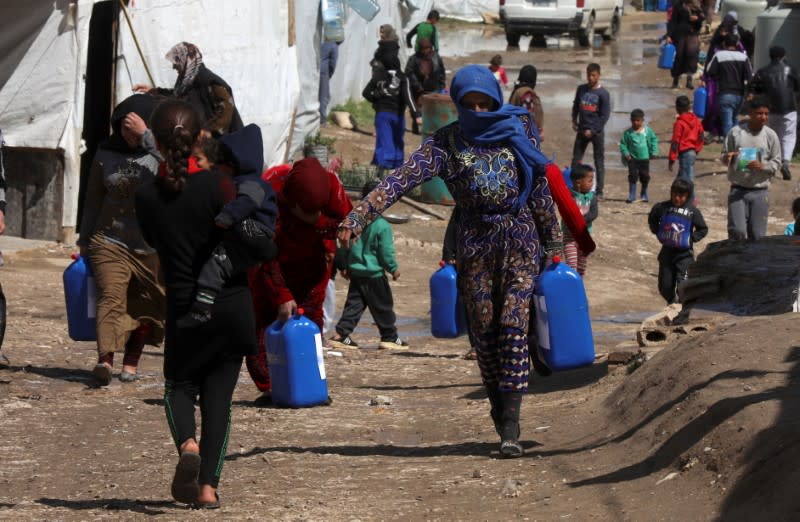 FILE PHOTO: Syrian refugees walk as they carry containers at an informal tented settlement in the Bekaa valley