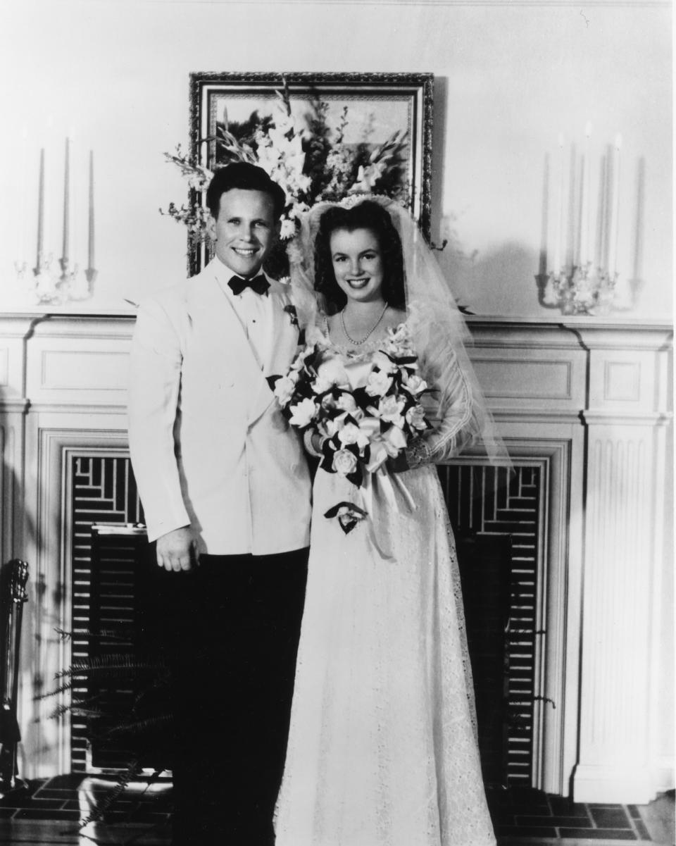 Bride in a long gown and groom in a tuxedo standing together, smiling at their wedding