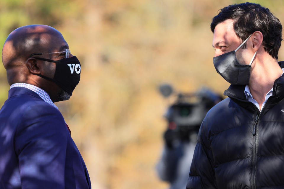 Rev. Raphael Warnock and Jon Ossoff, wearing face masks, face each other