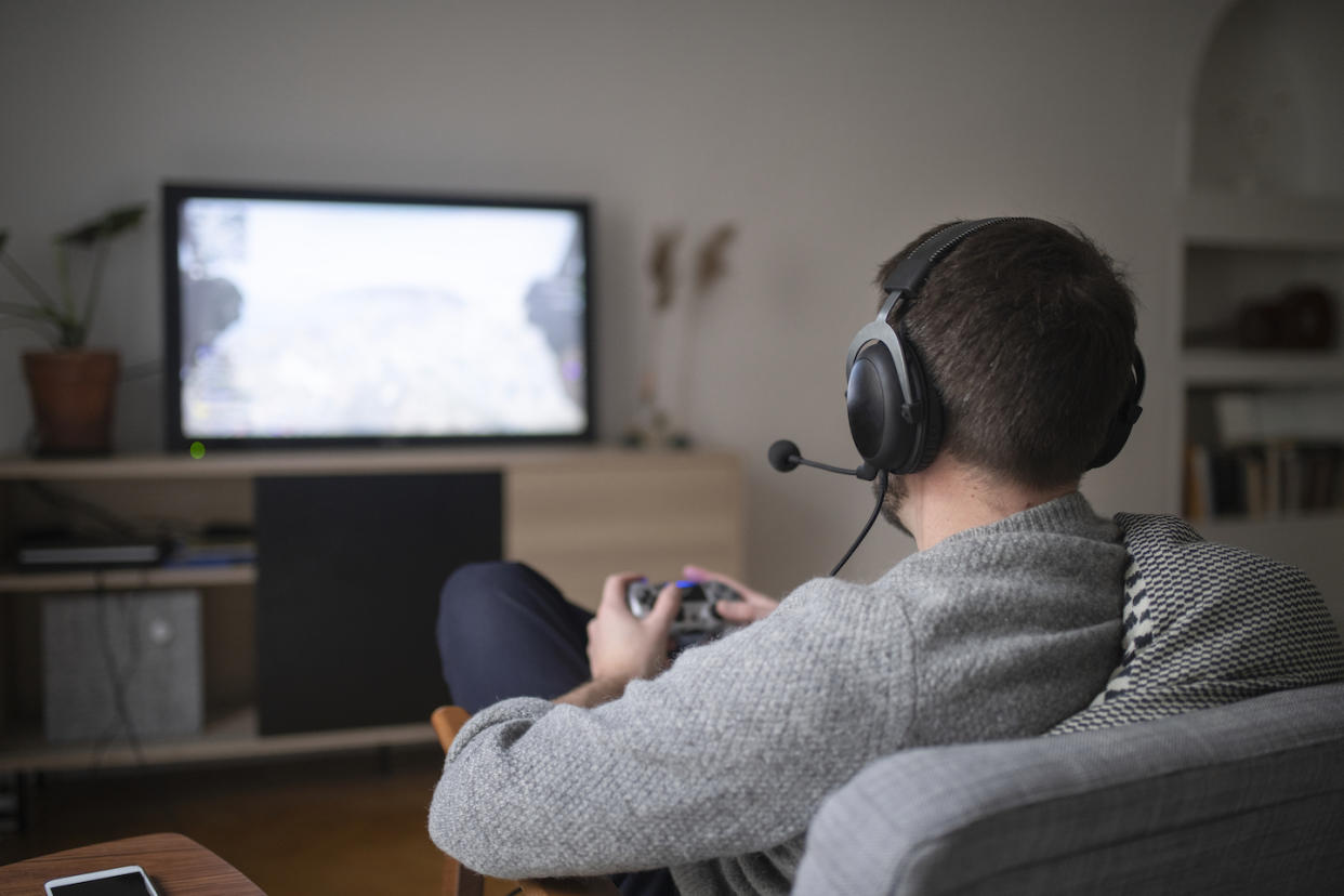 A gamer playing console games with a headset in front of a television in his living room. (Photo: Getty Images)