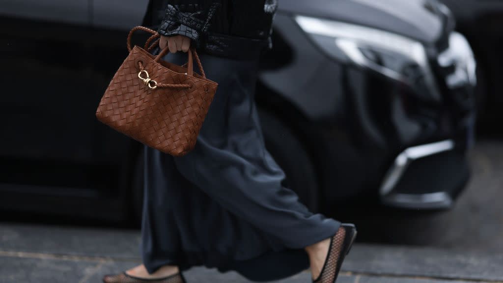 a woman carrying a brown leather andiamo tote bag by bottega veneta with a black jacket and silk skirt on the sidewalk in paris in a roundup of the best small tote bags 2024