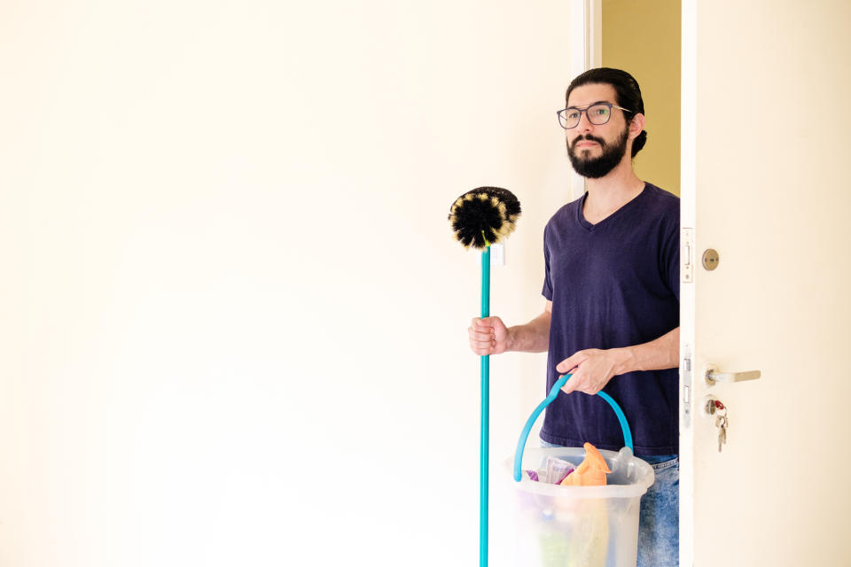 Man holding a mop and bucket, standing by an open door, looking surprised