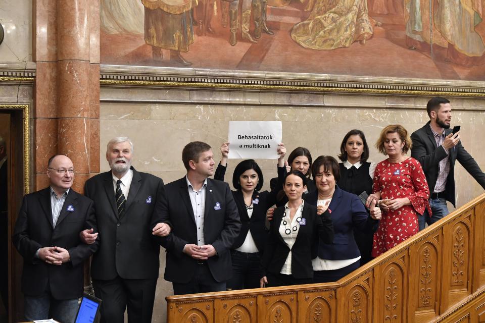 Deputy of the Hungarian Socialist Party (MSZP) Agnes Kunhalmi holds up a sheet that reads 'You succumbed to the multinational corporations' among other oppositional lawmakers as they block the steps leading to the rostrum at the start of the plenary session of the parliament in Budapest, Hungary, Wednesday, Dec. 12, 2018. (Lajos Soos/MTI via AP)