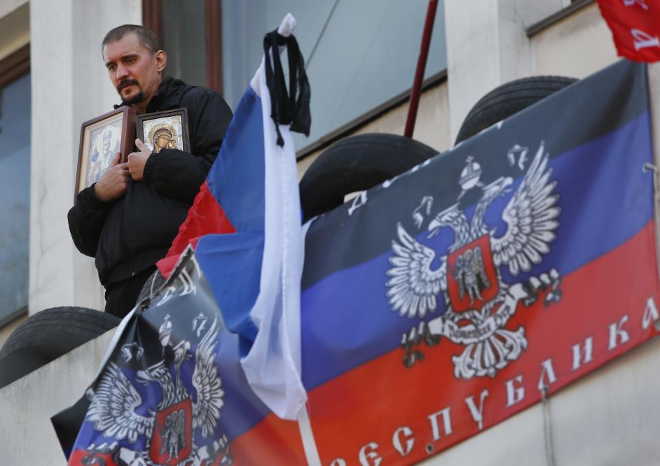 A pro-Russian protester holds icons as he stands outside a city hall bearing flags representing the Donetsk Republic in Mariupol, Ukraine, Thursday, April 17, 2014. Three pro-Russian protesters were killed and 13 injured during an attempted raid overnight on a Ukrainian National Guard base in the Black Sea port of Mariupol, Ukraine's authorities said Wednesday. (AP Photo/Sergei Grits)