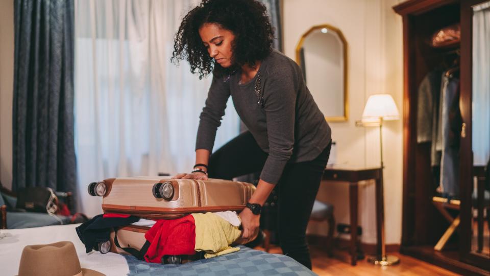 Mixed race woman unable to close suitcase before leaving the hotel room.