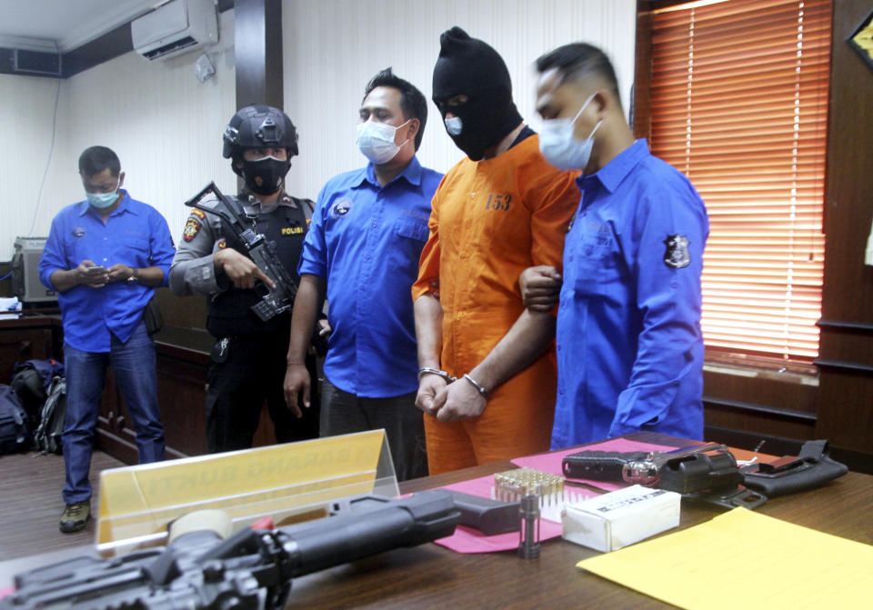 Police officers escort French national Rayan Jawad Hendri Bitar, center, as he is shown to the media along with the firearms confiscated from him, during a news conference at the Regional Police headquarters in Denpasar, Bali, Indonesia, Wednesday, Dec. 23, 2020. Indonesian police said Wednesday that they have arrested the Frenchman for allegedly possessing illegal guns and drugs on the resort island. (AP Photo/Zul Trionggono Edoardo)