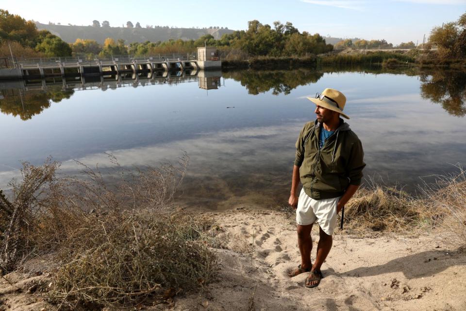 A man stands beside a river weir.