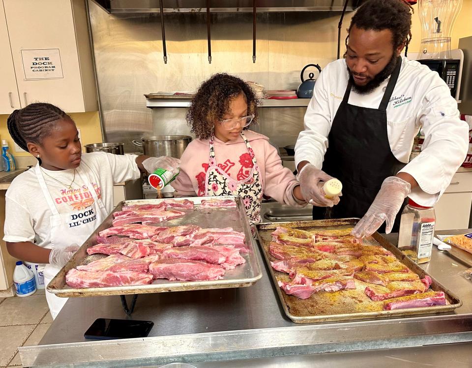 Trinity Johnson, 9, and Sanyah Pino, 11, learn the basics of seasoning meat from Chef Kamal Philibert in the kitchen at the Dorcas Outreach Center for Kids – The DOCK -- in Melbourne’s Booker T. Washington neighborhood.