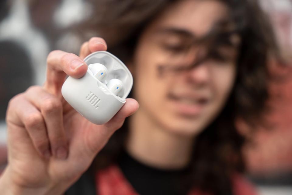 A young man holding white JBL Tune Flex earbuds.