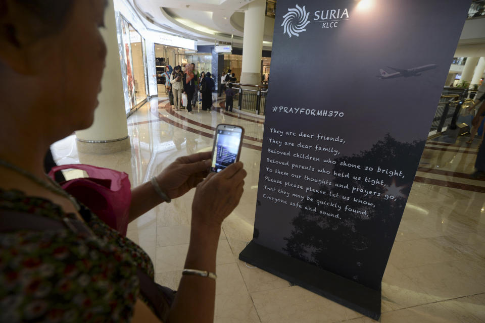A Malaysian Chinese woman takes pictures of a message board for the missing Malaysia Airline, Flight MH370 with a mobile phone camera at a shopping mall in Kuala Lumpur, Malaysia, Monday, March 24, 2014. A Chinese plane on Monday spotted two white, square-shaped objects in an area identified by satellite imagery as containing possible debris from the missing Malaysian airliner, while the United States separately prepared to send a specialized device that can locate black boxes. (AP Photo/Joshua Paul)