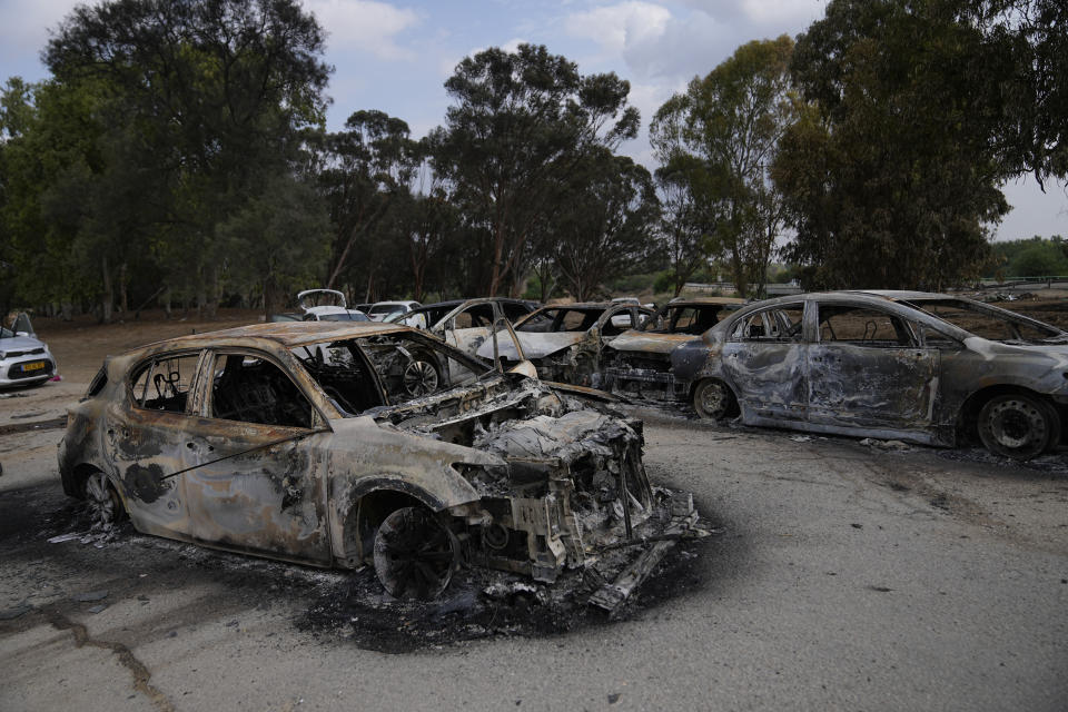Burned out cars in front of a cluster of trees.