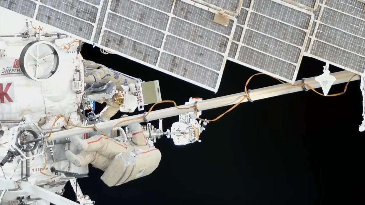  Two cosmonauts in white spacesuits work outside the international space station. 