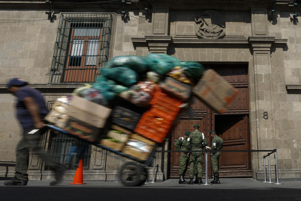 A man pulls a cart full of merchandise past the National Palace, as military police stand guard during a private meeting between U.S. Attorney General William Barr and Mexico's President Andres Manuel Lopez Obrador, in Mexico City, Thursday, Dec. 5, 2019. The two met behind closed doors Thursday, about a week after U.S. President Donald Trump suggested his government could classify Mexican drug cartels as terrorist organizations. (AP Photo/Rebecca Blackwell)