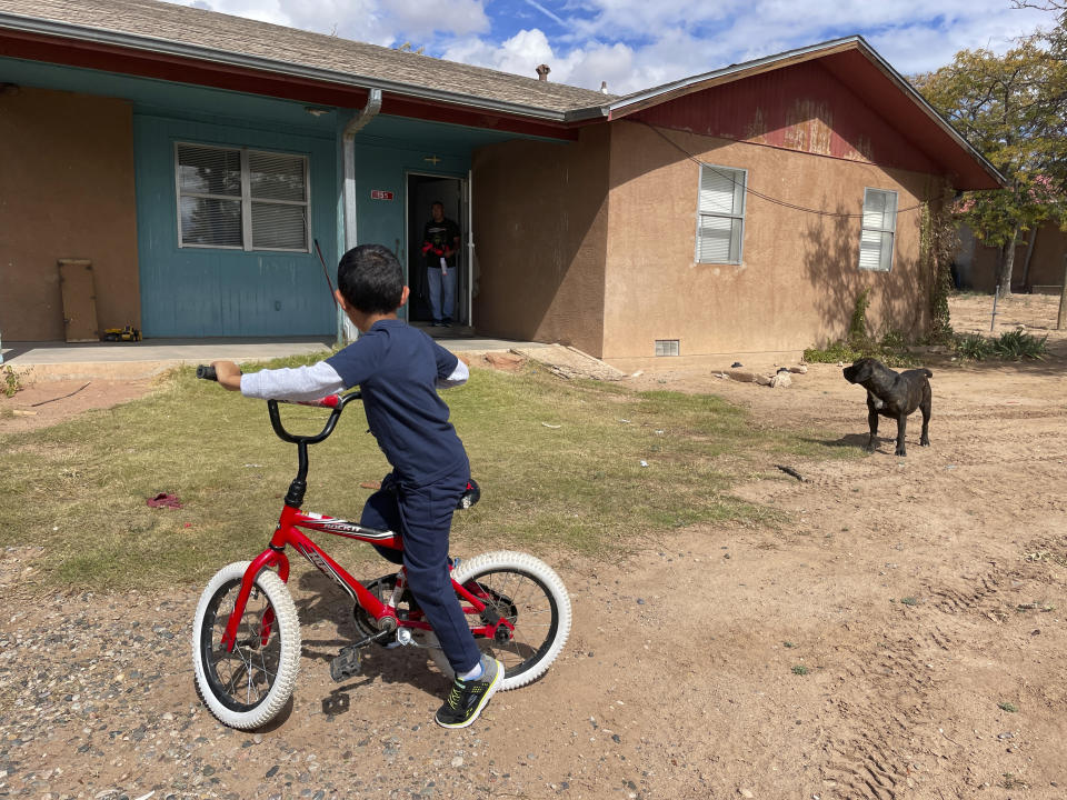 Micca Madalena rides his bicycle in his front yard as his father, Darryl Madalena, watches from the doorway of their home at Jemez Pueblo, N.M., Oct. 7, 2022. Micca's mother died after getting a growth removed from her liver. Getting on a transplant list was never discussed, and now Darryl Madalena is advocating for more Native Americans to consider joining the organ donation rolls. (AP Photo/Susan Montoya Bryan)