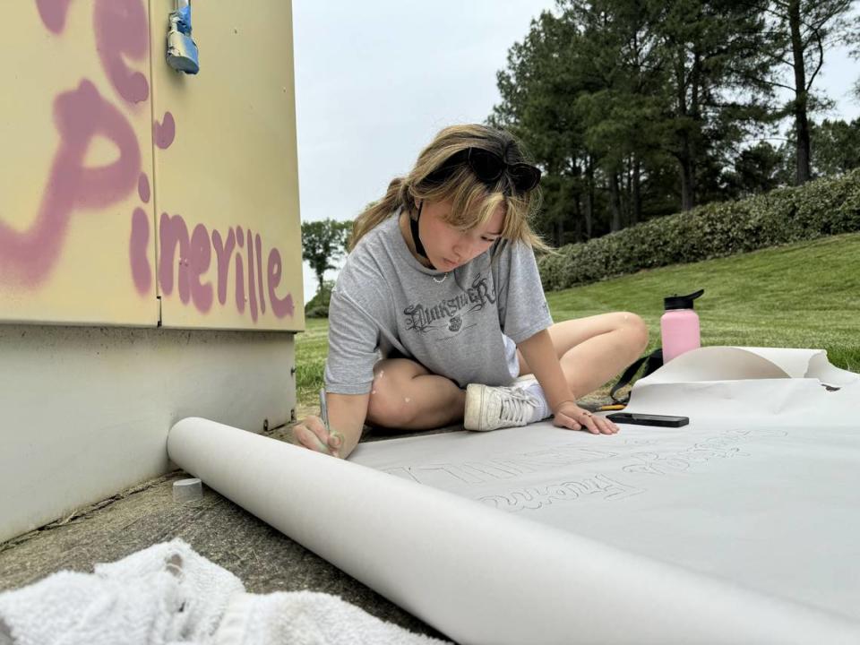 Art student Sophie Romine prepares a stencil for a utility box at Pineville Lake Park.