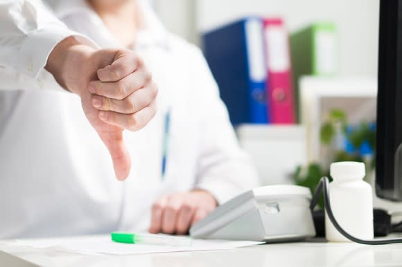 Doctor sitting in office with his thumb pointing down.