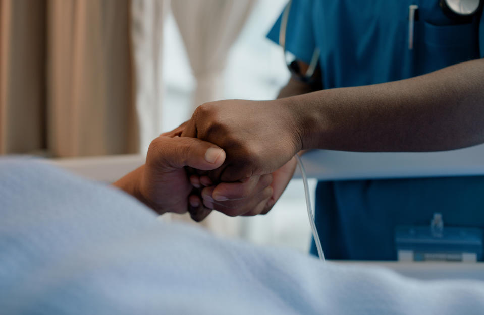 A healthcare worker holding a patient's hand, offering comfort and support