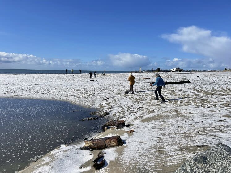 People walk along a snow covered Twin Lakes State Beach in Santa Cruz, Calif., on Thursday, Feb. 23, 2023. (Karen Krenis via AP)