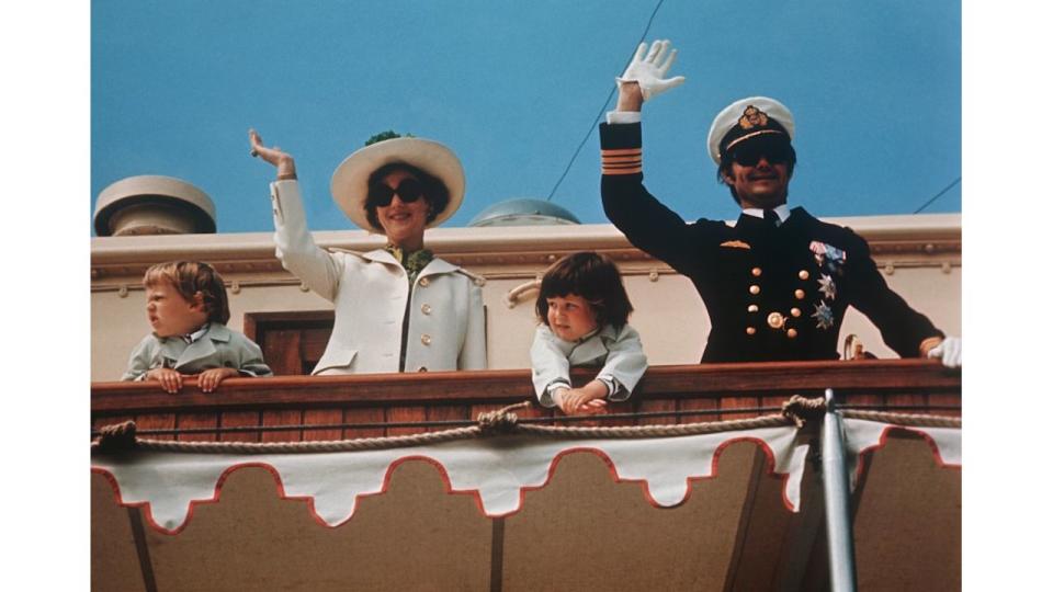 A young Prince Joachim and King Frederik with their parents Queen Margrethe and Prince Henrik waving from a yacht