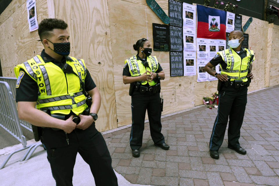 FILE - In this June 6, 2020, file photo, Boston Police officers stand in front of messages about George Floyd posted on a boarded-up business in Downtown Crossing in Boston. The city's police department remains largely white, despite vows for years by city leaders to work toward making the police force look more like the community it serves. Advocates say Black and Latino candidates still consistently get passed over in favor of white applicants. (AP Photo/Michael Dwyer, File)