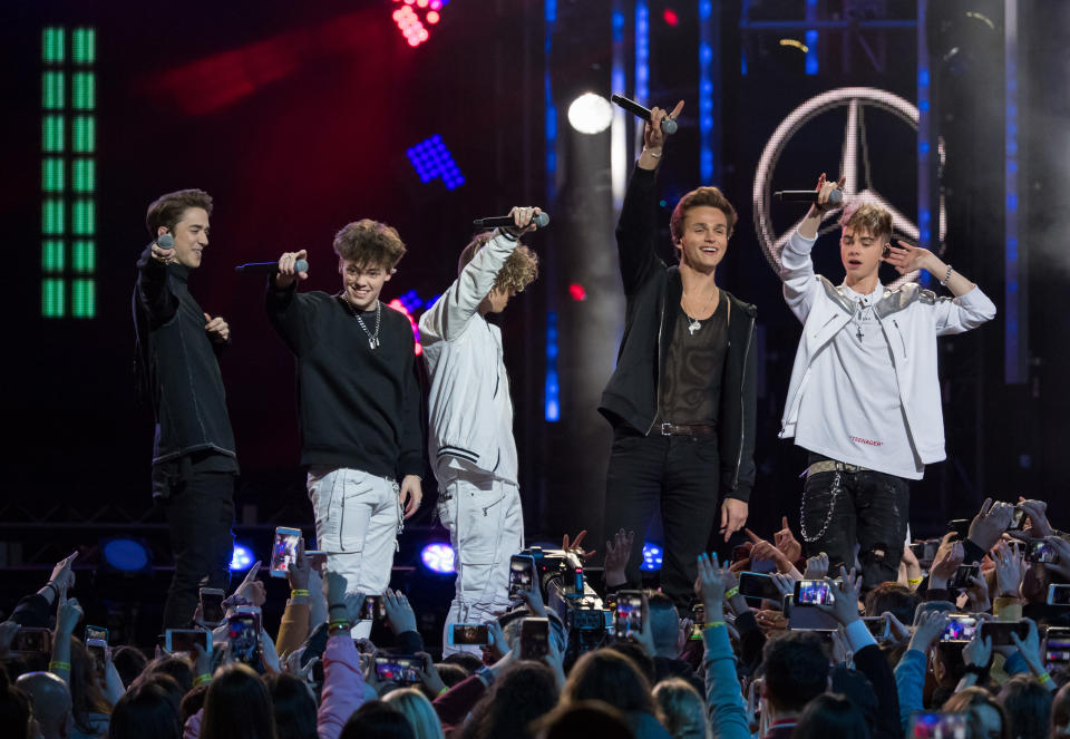 The band smile and hold their microphones in the air on stage