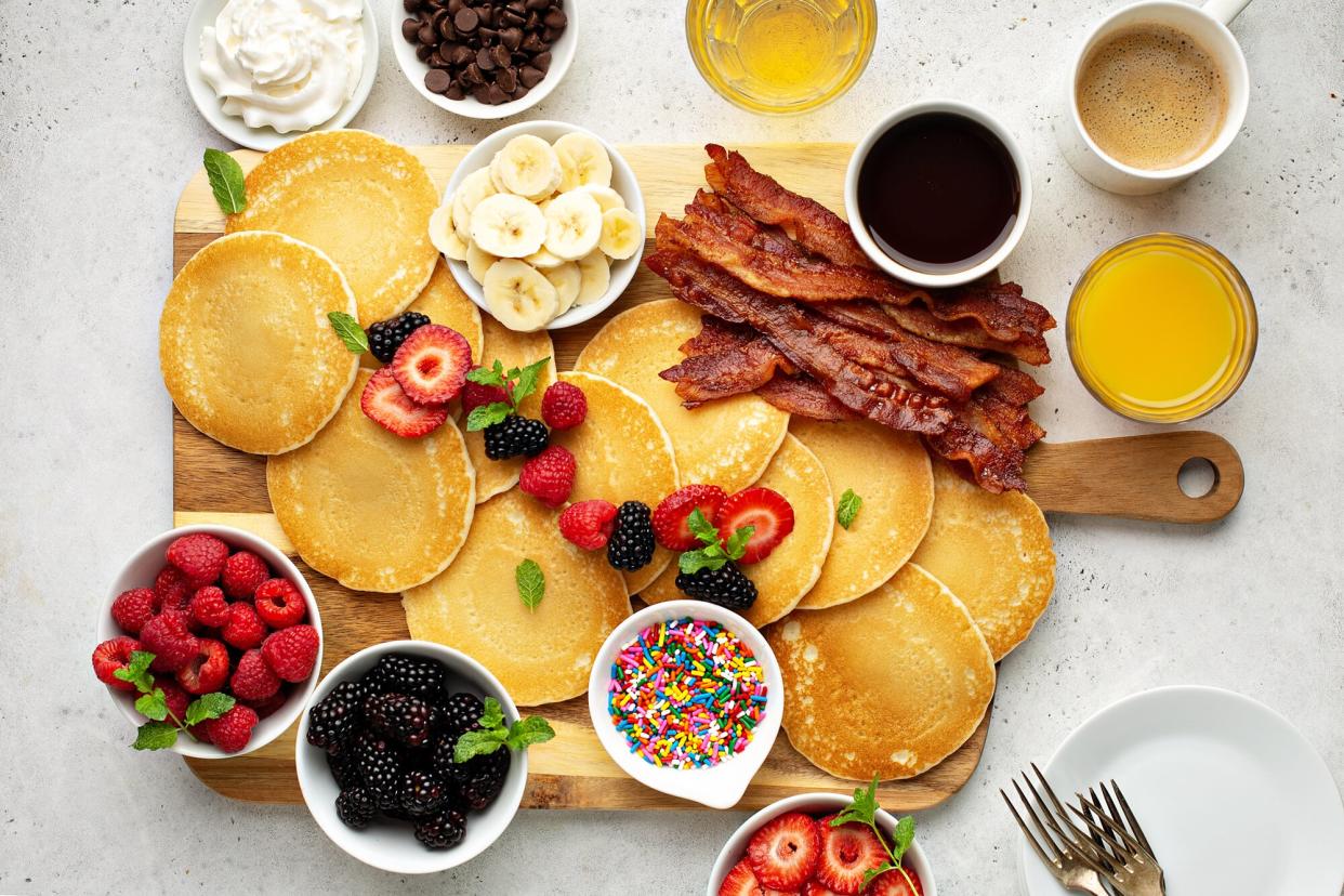 Big pancake breakfast table with berries, bacon and maple syrup