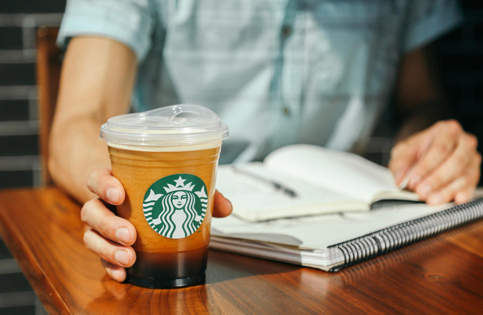 A man sitting at a table looking at a book and holding a Starbucks cup.