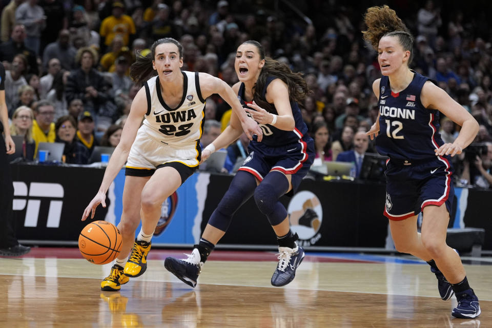 Iowa guard Caitlin Clark (22) drives to the basket past UConn guard Nika Muhl (10) and guard Ashlynn Shade (12) during the second half of a Final Four college basketball game in the women's NCAA Tournament, Friday, April 5, 2024, in Cleveland. (AP Photo/Morry Gash)