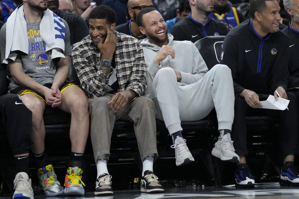 Golden State Warriors' Gary Payton II, middle left, laughs on the bench next to Stephen Curry during the first half of the team's NBA basketball game against the Los Angeles Clippers in San Francisco, Thursday, March 2, 2023. (AP Photo/Jeff Chiu)