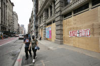 Pedestrians pass a boarded up storefront, Wednesday, June 3, 2020, in the SoHo neighborhood of New York. Graffiti on the boarded up store reads "Justice 4 Floyd." Protesters broke into nearby stores Tuesday night in reaction to George Floyd's death after he was restrained while in police custody on May 25 in Minneapolis. (AP Photo/Mark Lennihan)