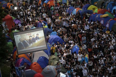 Pro-democracy protesters watch formal talks between student protest leaders and government officials on a video screen near the government headquarters in Hong Kong in this October 21, 2014 file photo. REUTERS/Carlos Barria/Files
