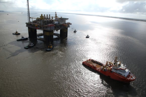 Offshore drilling rig with service vessel and small craft right next to it on the open water near sunrise or sunset.