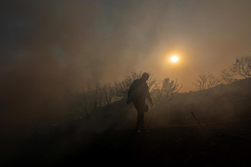 A police officer is silhouetted as a wildfire burns on Rhodes.